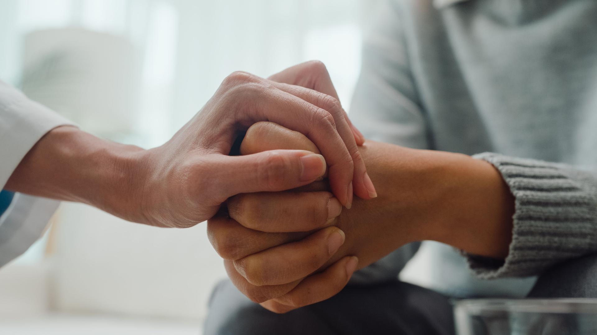 Closeup of young Asian female psychotherapist discussing a problem and touch hand young depressed sit on couch at clinic. Medical insurance, Mental health.